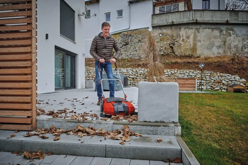 Person entfernt Laub mit Handkehrmaschine